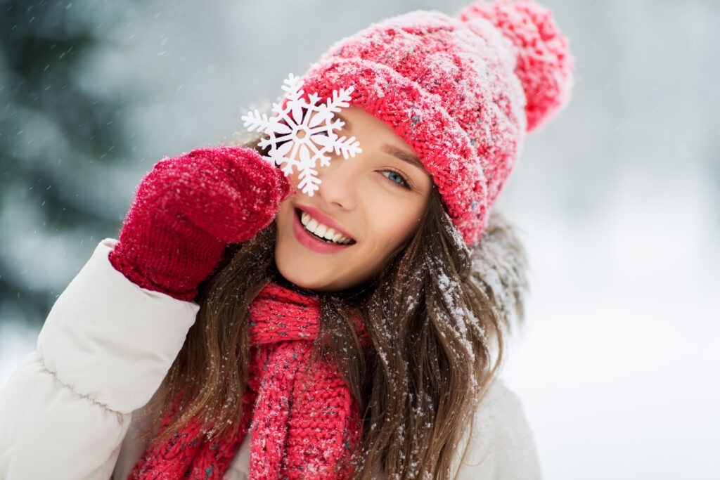 woman wearing red winter clothing holding a snowflake up to her eye.